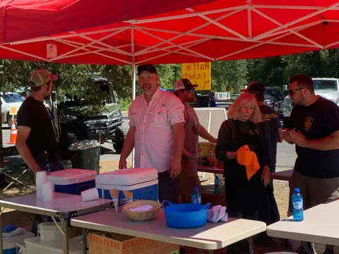 People stand and work behind tables under a red canopy tent outdoors.