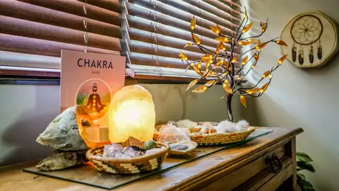 An interior view of a wooden surface displaying crystals, a salt lamp, a chakra guide, and a decorative tree with lights.