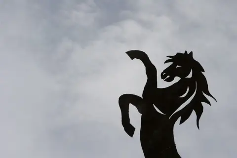 A silhouette of a rearing horse against a cloudy sky.