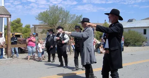 Men in historical costumes point down a street while spectators watch.