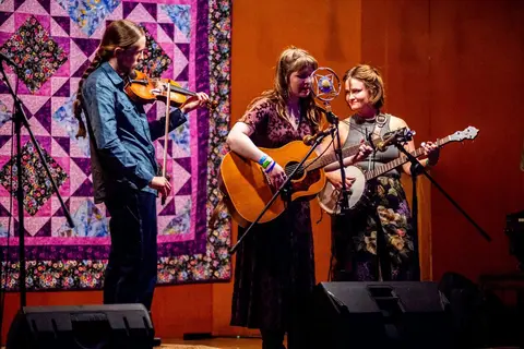 Three musicians perform on stage with instruments.