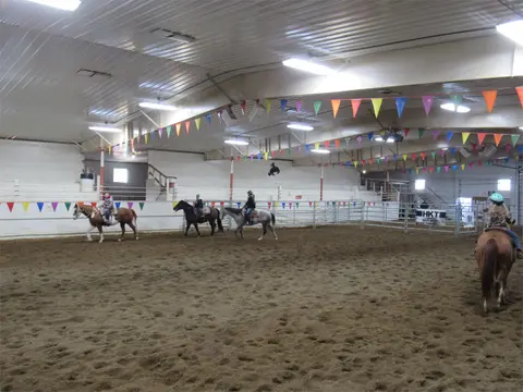 People ride horses inside an indoor dirt arena decorated with colorful pennants.