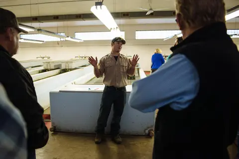 A guide speaks to visitors inside an industrial interior with large tanks.