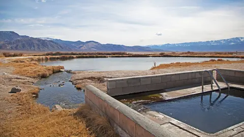 A concrete pool with metal handrails sits beside a natural pond and mountains.