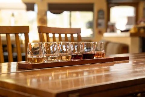 A flight of glasses containing various drinks stands on a wooden table inside.
