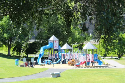 A colorful playground sits in a green park with trees and paths.