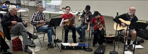 A group of people sit in a circle playing musical instruments indoors.
