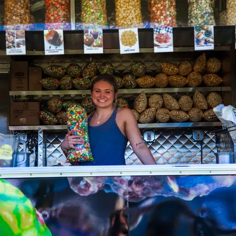 A smiling woman holds a bag of colorful popcorn inside a concession stand.