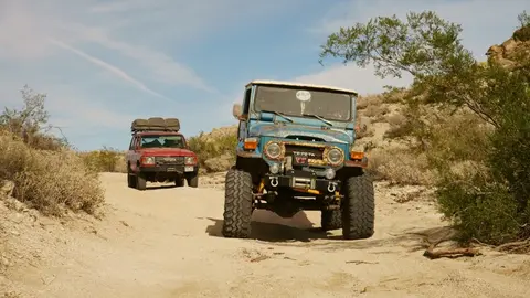 Two off-road vehicles driving on a dirt trail in a landscape.