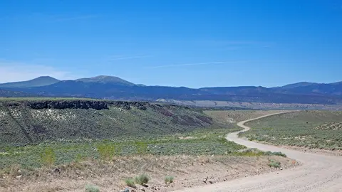 A winding dirt road cuts through a vast desert landscape under a clear blue sky.