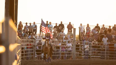 A person on horseback holding an American flag in front of a crowd of spectators.