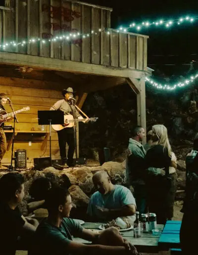 A country band plays on a wooden stage outdoors at night while people watch and dance.