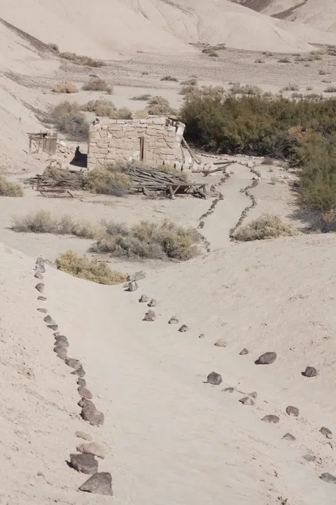 A stone structure sits in an arid landscape with a path lined by rocks.