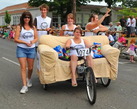 People participate in a street event riding a couch tricycle.