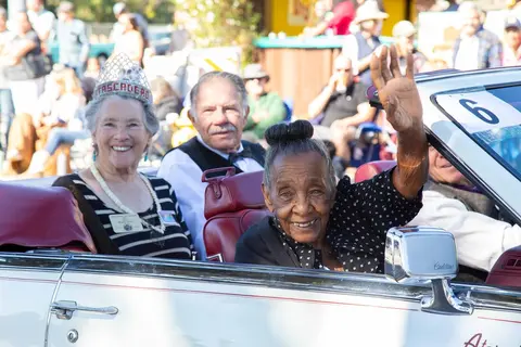 People ride in a convertible during a parade.