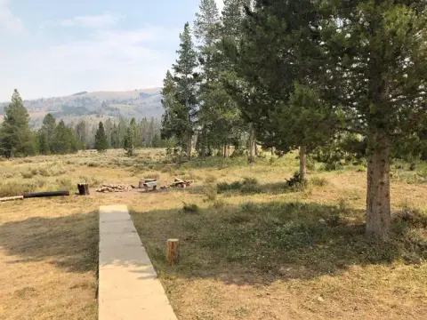 A concrete path leads through a grassy area with trees and distant hills.