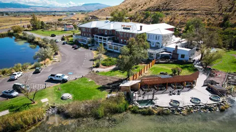 An aerial view of a large historic hotel building with hot springs and a lake next to it.