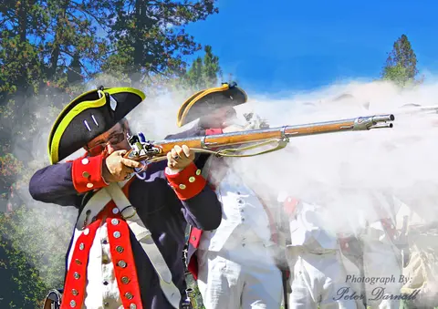 Men in historical military uniforms fire muskets outdoors.