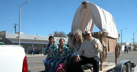 People posing on a covered wagon parade float.