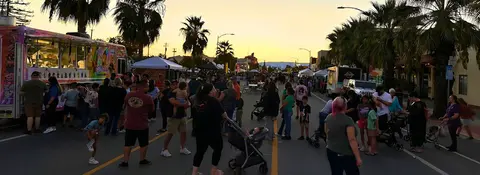 A street lined with food trucks and a crowd of people gathered for an event at dusk.
