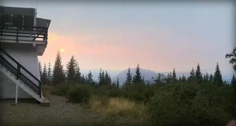 A view of a mountain landscape with a lookout tower and trees during sunset.