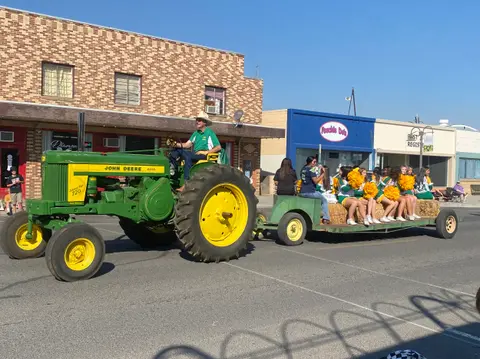 A John Deere tractor pulls a float with cheerleaders in a street parade.