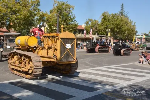 A vintage crawler tractor drives down a street in a parade.