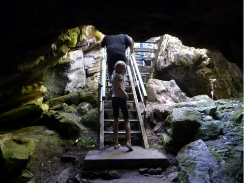 People walking up stairs inside a rocky cave opening.