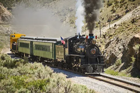 A steam train travels along tracks through a mountainous landscape.
