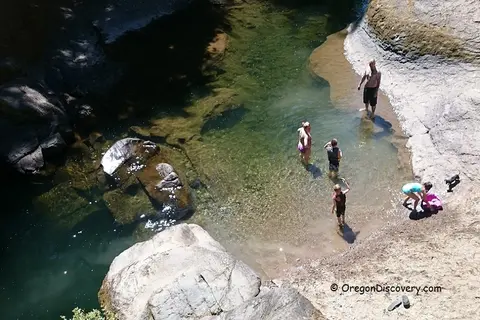 An overhead view of people swimming and wading in a rocky stream.
