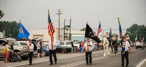 People carry flags and ride horses in a street parade.