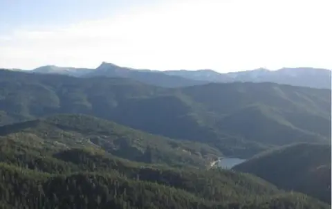 A wide view of forested mountains and hills under a bright sky.
