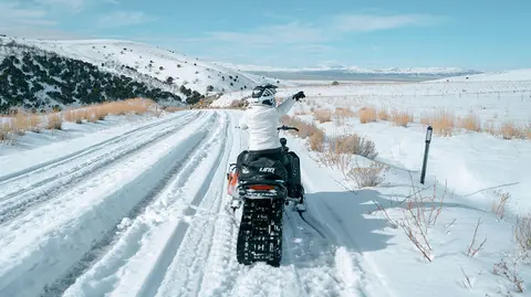 A person on a snowmobile points ahead on a snow-covered trail.