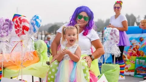 A young child in a colorful dress sits on a woman's lap at an outdoor event.