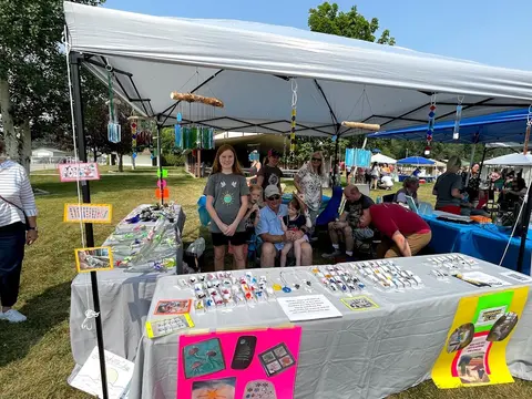 People at a craft booth under a tent outdoors.