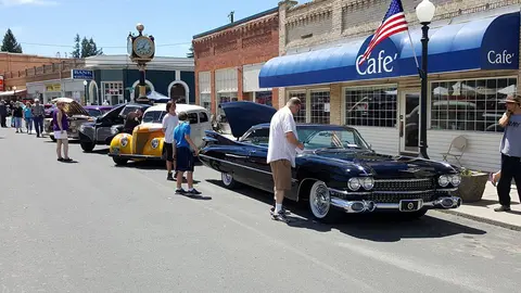 A street scene with classic cars parked along a building with a cafe awning.