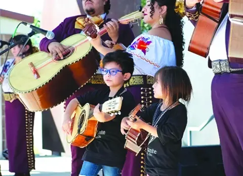 A group of musicians playing guitars alongside two young children holding small guitars.