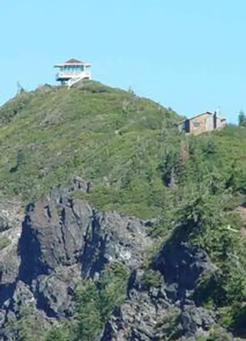 A structure sits on top of a grassy and rocky hill.