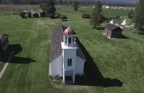 An aerial view shows a white church with a red cupola in a grassy field.