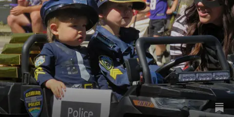 Two children in police costumes sit in a toy vehicle.
