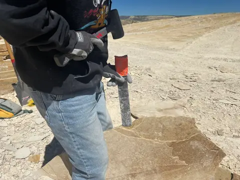 A person holds a hammer and chisel while splitting a rock outdoors.