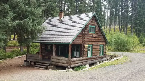 A log cabin sits in a forest next to a dirt road.