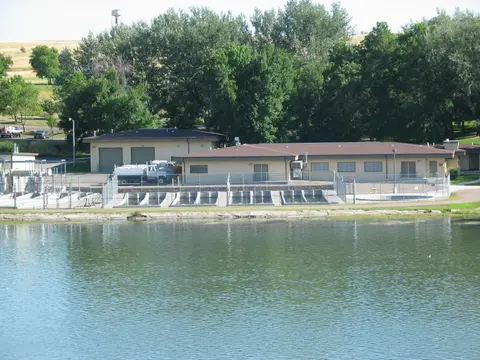 A water treatment facility sits next to a body of water, surrounded by trees.