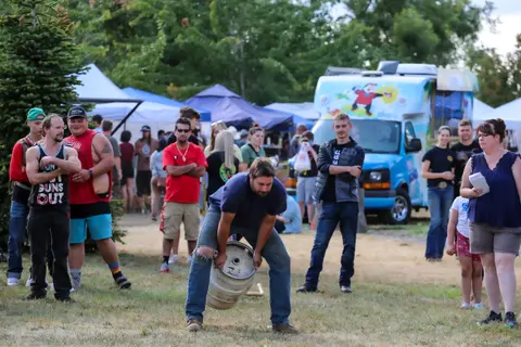 A man lifts a keg outdoors while people watch.