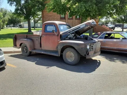 A rusty vintage pickup truck is parked outdoors with its hood open.