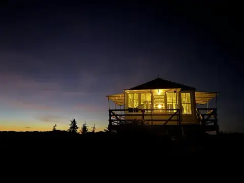 A brightly lit lookout tower stands against a twilight sky.
