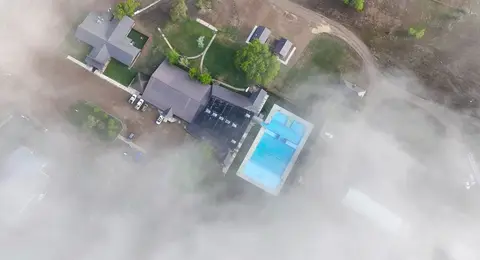 An aerial view shows buildings and a swimming pool partially obscured by fog.