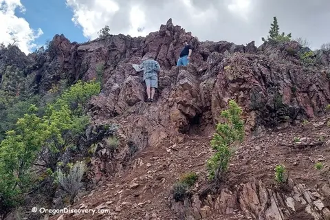Two people climbing a rocky hill outdoors.