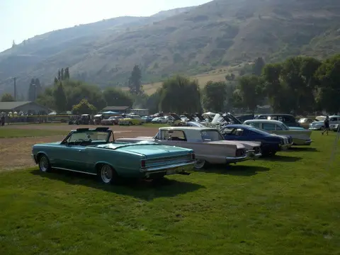Classic cars parked on a grassy field in front of a hilly landscape.