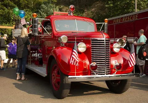 A vintage red fire truck is parked outdoors with people standing around it.